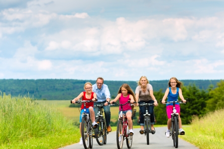 Family with three girls having a weekend excursion on their bikes on a summer day in beautiful landscape Family with three girls having a weekend excursion on their bikes on a summer day in beautiful landscape