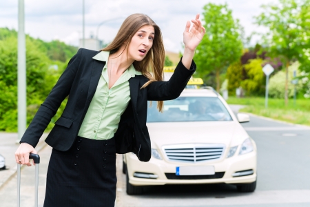 Young businesswoman waiting for a taxi stopping the driver waving from the sidewalkの写真素材