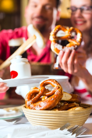 Young people in traditional Bavarian Tracht eating with sausages in restaurant or pub lunch or dinnerの写真素材