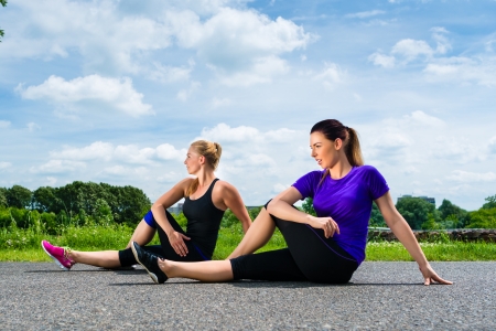 Urban sports - young women doing warming up together before running in the greenfield on a summer dayの写真素材