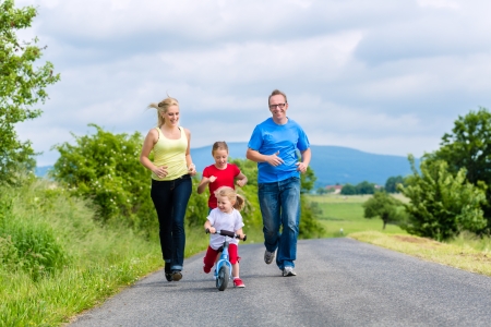 Family of Little girl father and mother or mom and dad running on street in rural environment for sportの写真素材
