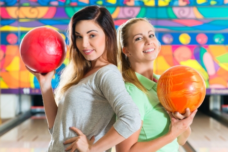 Young people or friends, man and women, playing bowling with a ball in front of the ten pin alley, they are a teamの写真素材