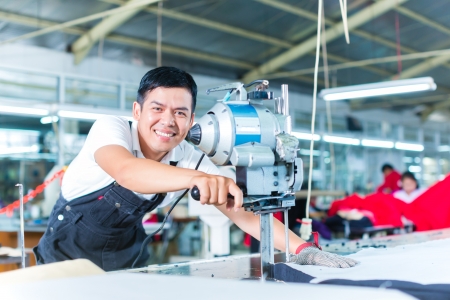 Indonesian worker using a cutter - a large machine for cutting fabrics - in a asian textile factory, he wears a chain gloveの写真素材