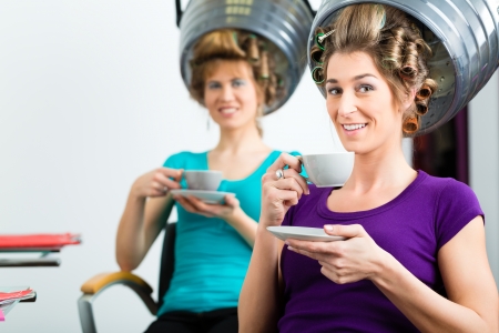 women at the hairdresser drinking coffee or cappuccino and chit-chat, while your hair drying under a hairdryerの写真素材