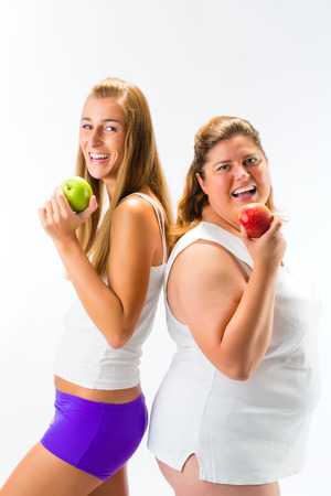 Thin and fat or obese woman standing and holding an apple in hand, studio shot isolated on whiteの写真素材