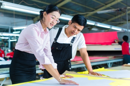 Indonesian Worker or foreman and dressmaker, tailor or designer looking at pattern on a table in a Asian textile factoryの写真素材