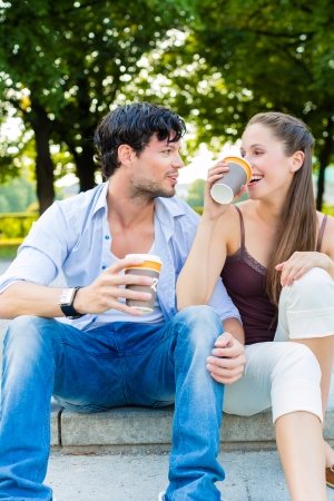 Man and woman or young couple drinking coffee and sitting in city park in summer on stairsの写真素材