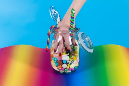 Young woman with many unhealthy sweets or candy in Studio, she have a sweet tooth and grabbing some goodies out of a glassの写真素材