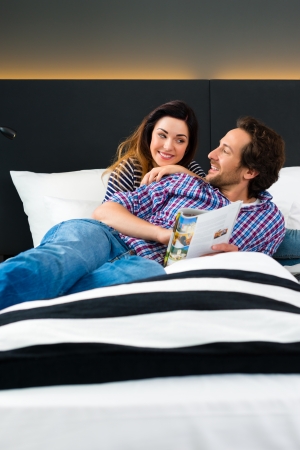 Young Couple lying in the bed of a hotel room, they are on vacation and using the wi-fi in the room for internet with the computerの写真素材