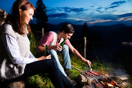 Tyrol - Young couple sitting on alpine meadow of a mountain on Campfire in the Bavarian Alps enjoying the romantic evening sunset of the panorama in leisure time or vacationの写真素材