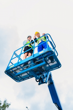 Construction workers on site in hydraulic lifting ramp discussing the project on pad or tablet computerの写真素材