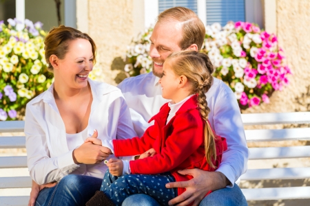 Family with mother, father and daughter together on garden bench in front of homeの写真素材