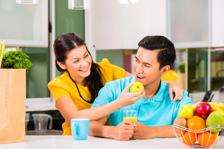 Young Asian Couple handsome woman feeding boyfriend with apple after grocery shoppingの写真素材