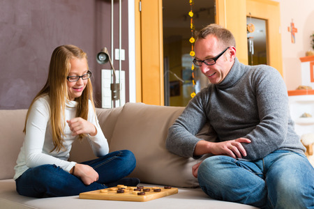 Father and daughter playing parlor or board game checkers on sofaの写真素材