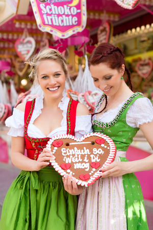 Young women in traditional Bavarian clothes - dirndl or tracht -with a gingerbread souvenir heart on a festival or Oktoberfestの写真素材