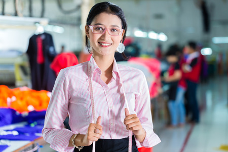 Female Indonesian tailor, dressmaker or designer standing proudly in an Asian textile factory, it is...