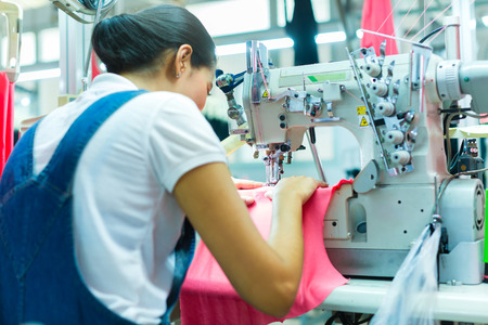 Asian Seamstress or worker in an Asian textile factory sewing with a industrial sewing machine, she is very accurateの写真素材
