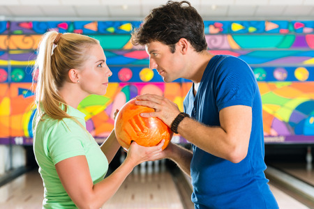 Young couple or friends, man and woman, playing bowling with a ball in front of the ten pin alley, they are a teamの写真素材