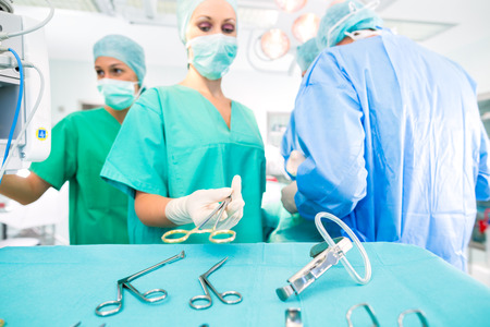 Hospital - surgery team in the operating room or Op of a clinic operating on a patient, perhaps it's an emergency a assistant holding a cotton swap forcepsの写真素材