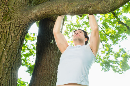 Young man exercising chins or pull ups in City Park under summer trees for sport fitness
