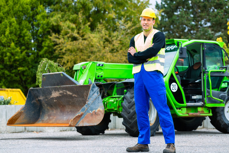 Builder or driver standing in front of construction machinery on building site