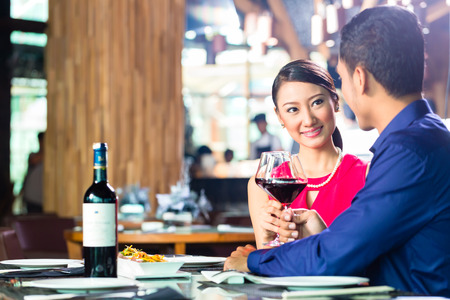 Asian couple having dinner and drinking red wine in very fancy restaurant with open kitchen の写真素材