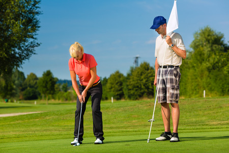 Young sportive couple playing golf on a golf course, she is putting at the greenの写真素材