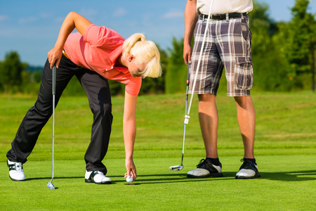 Young sportive couple playing golf on a golf course, she takes the ball from the holeの写真素材
