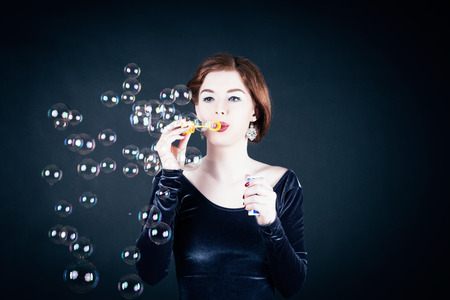 Girl making soap bubbles in front of dark background