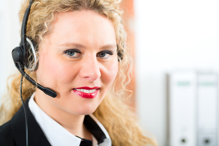 Young businesswoman or secretary working in her Office, she sitting on the desk in front of the window and working on a computer with a headset, she has a customer pitchの写真素材