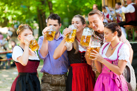 In Beer garden in Bavaria, Germany - friends in Tracht, Dirndl and Lederhosen and Dirndl standing in front of bandの写真素材