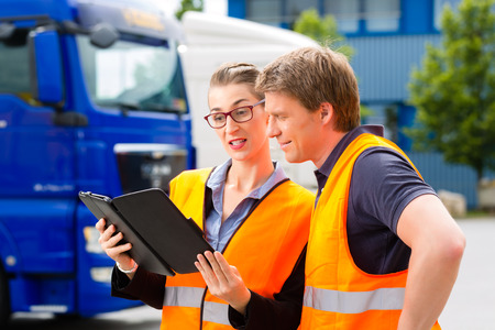 Logistics - proud driver or forwarder and female coworker with tablet computer, in front of trucks...
