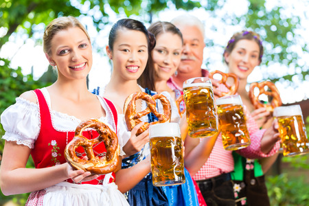 In Beer garden - friends, man and women in Tracht, Dirndl and Lederhosen drinking a fresh beer in Bavaria, Germanyの写真素材