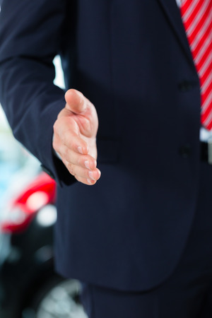 Seller or car salesman in car dealership presenting his new and used cars in the showroomの写真素材