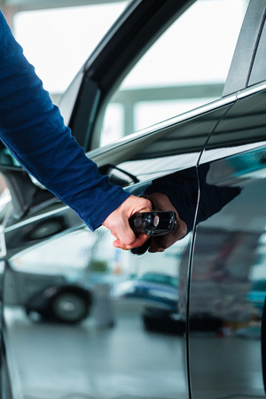 Young man beside a new car in car dealership, obviously he is buying the auto, or making a test driveの写真素材
