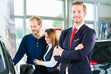 Seller or car salesman and clients or customers in car dealership presenting the interior decoration of new and used cars in the showroomの写真素材