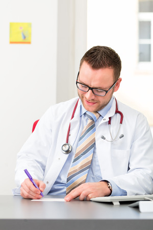 Young doctor writing medical prescription in surgery at deskの写真素材