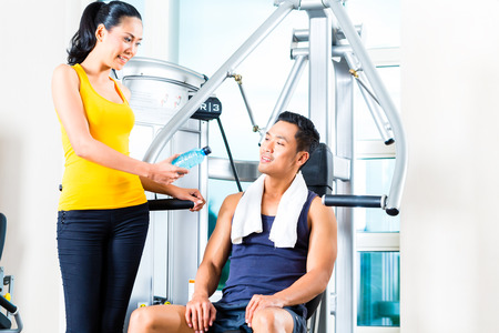 Woman passing bottle of water to man at gym