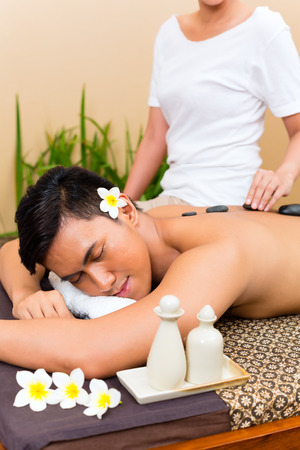 Indonesian Asian man in wellness beauty day spa having hot stone massage or treatment, looking relaxedの写真素材