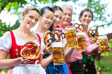 In Beer garden - friends, man and women in Tracht, Dirndl and Lederhosen drinking a fresh beer in Bavaria, Germanyの写真素材