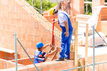 Two builder or worker with helmets controlling walls in scaffold with a bubble level on building or...