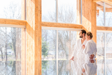 Couple on pool looking relaxed throw window of wellness spa wearing bath robeの写真素材