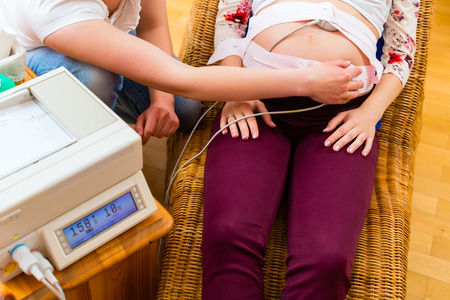 Midwife exanimating belly of pregnant woman with CTG scanning in practiceの写真素材