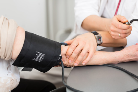 Young female doctor measuring blood pressure of senior patient in surgery consultation hour