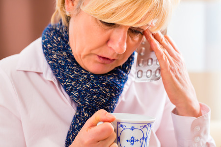 Old woman drinking tea to cure her bad cold or flu at homeの写真素材