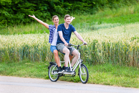 Man and woman, a couple,  riding together tandem bike on country laneの写真素材