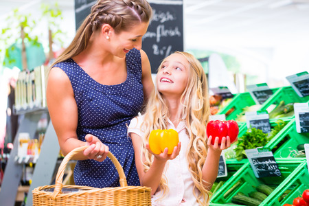 Mother and daughter selecting vegetables while grocery shopping in organic supermarketの写真素材
