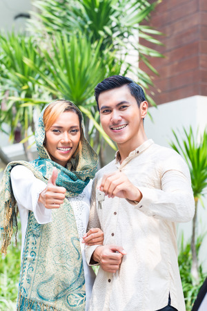 Asian Muslim man and woman moving into house presenting latchkey or keyの写真素材