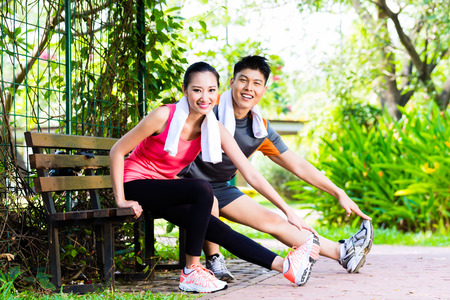 Asian Chinese man and woman stretching muscles on park benchの写真素材