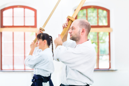 Man and woman fighting with wooden swords at Aikido training in martial arts schoolの写真素材